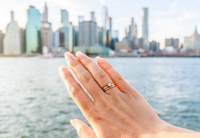 Young woman's hand with diamond engagement ring solitaire, gold wedding band.