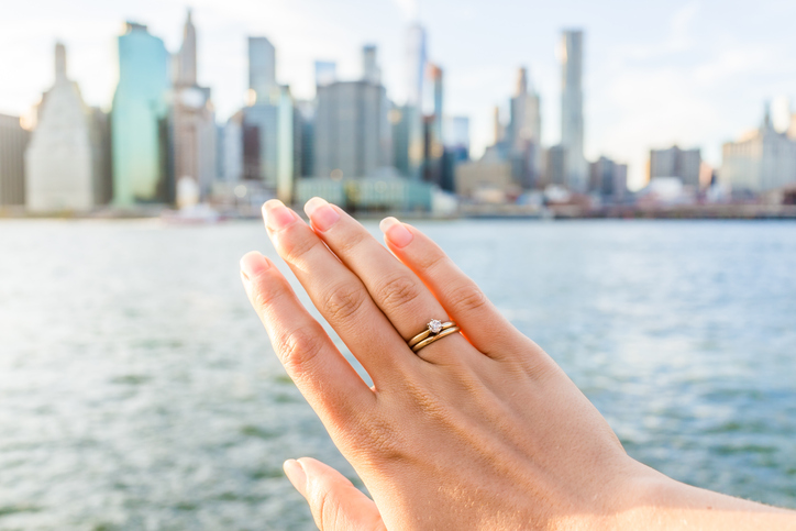 Young woman's hand with diamond engagement ring solitaire, gold wedding band.